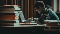 Osoba studiująca z laptopem i książkami przed sobą, reprezentująca przygotowanie wymagane do zdania egzaminu CompTIA Security+ Certification Exam.